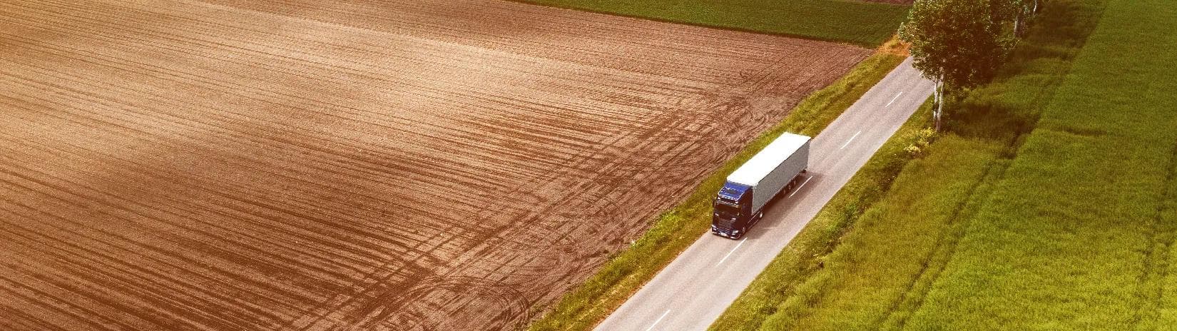 An 18-wheeler truck driving in the country in the summer. 