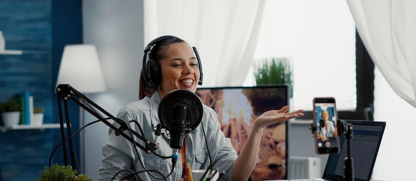 A young influencer with headphones on records a video with a smartphone while talking to her audience.