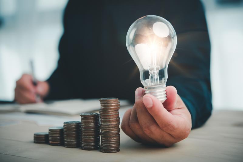 Man holding lightbulb next to stacks of coins