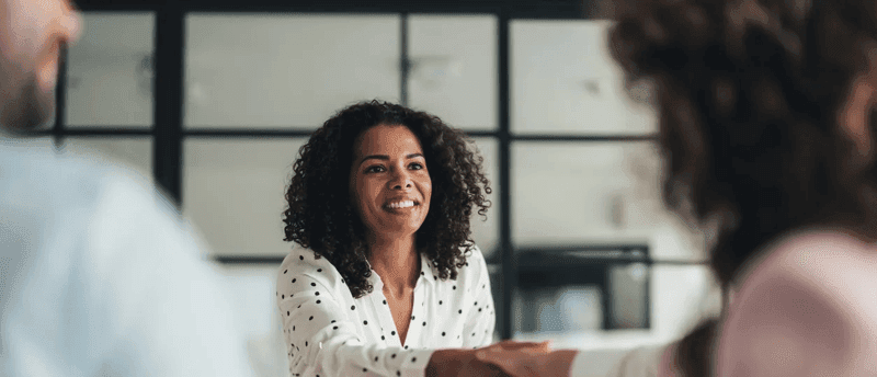 A woman manager shakes hands over a table, signifying a successful business transaction.