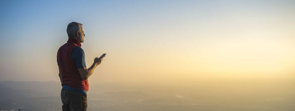Man overlooking cliff with phone in hand