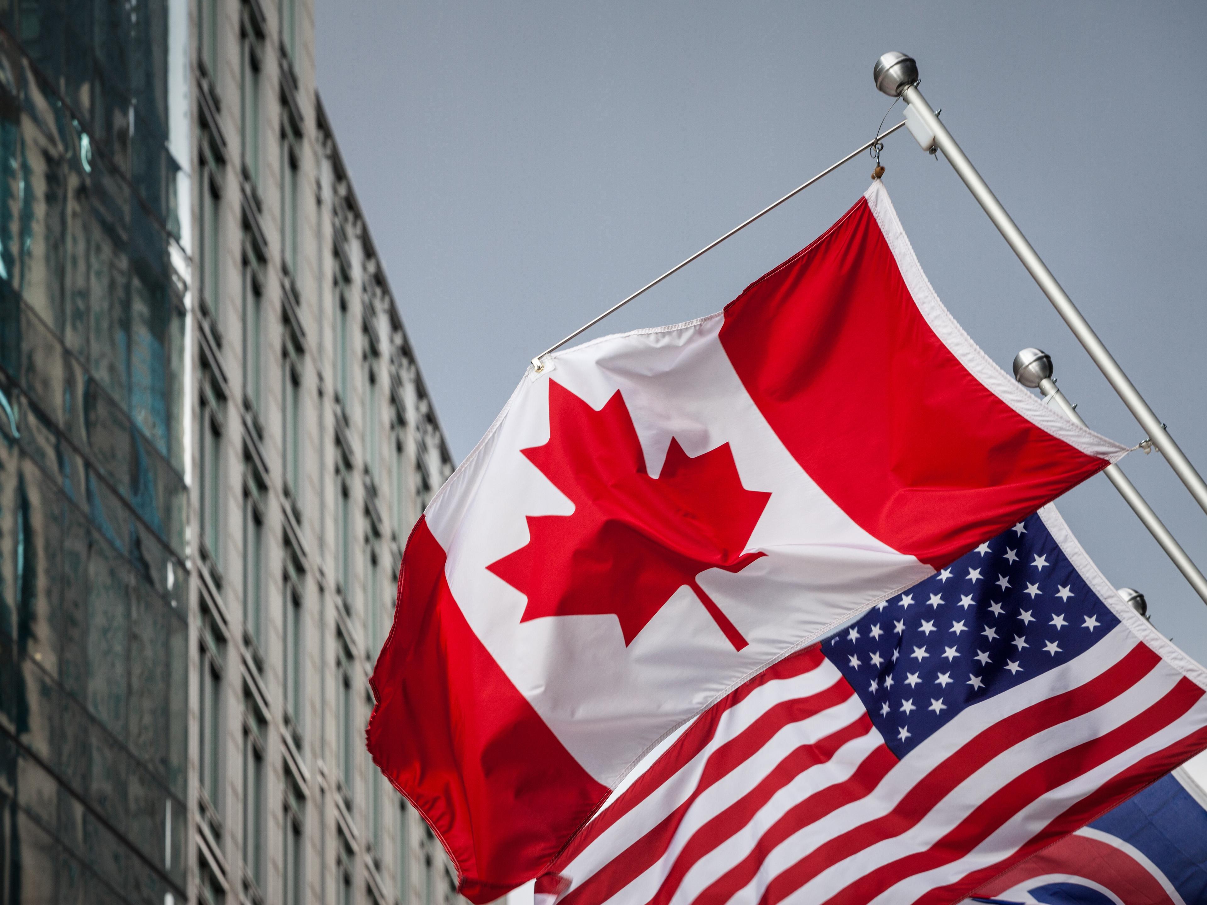 Canadian and US flag flying in front of downtown building