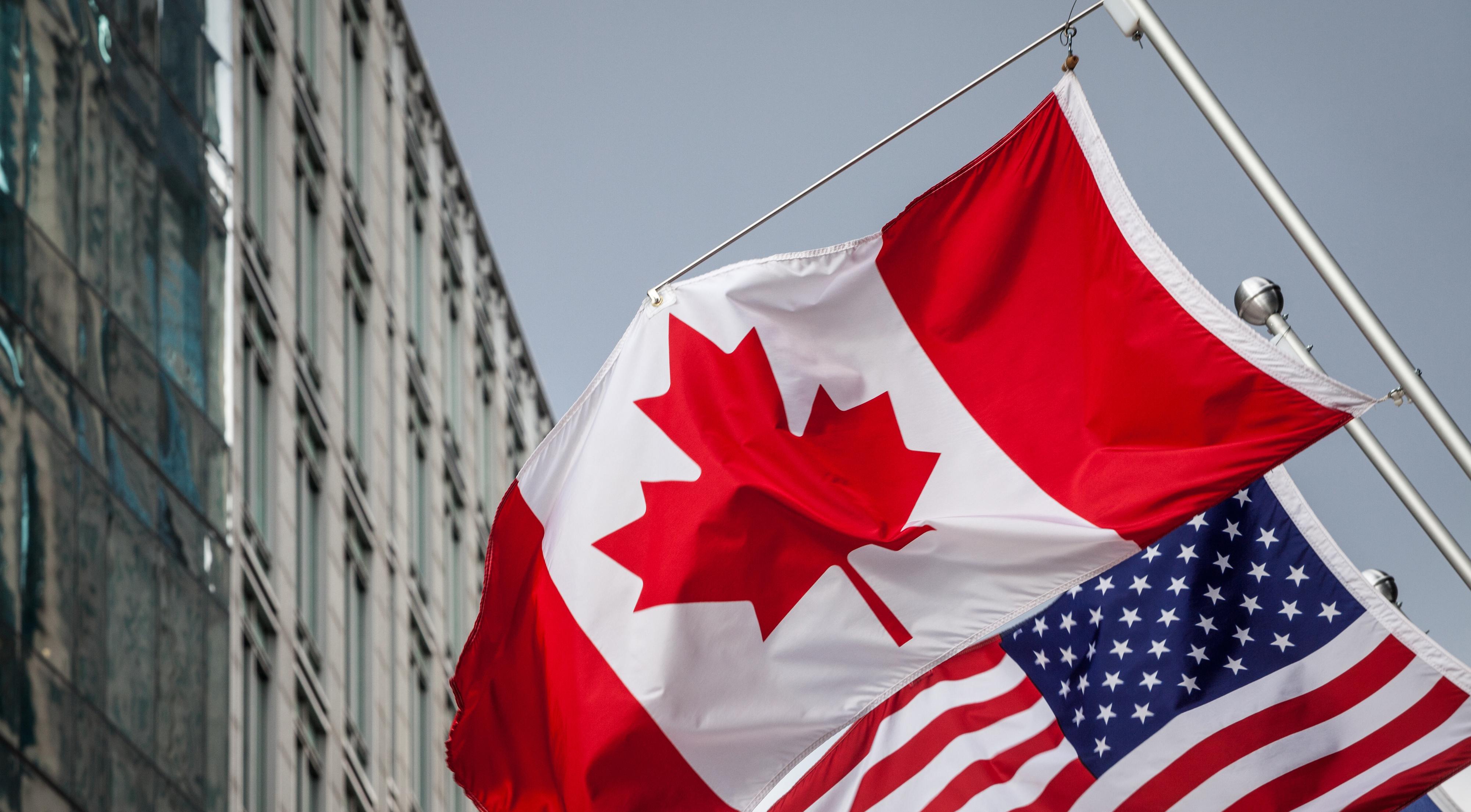 Canadian and US flag flying in front of downtown building