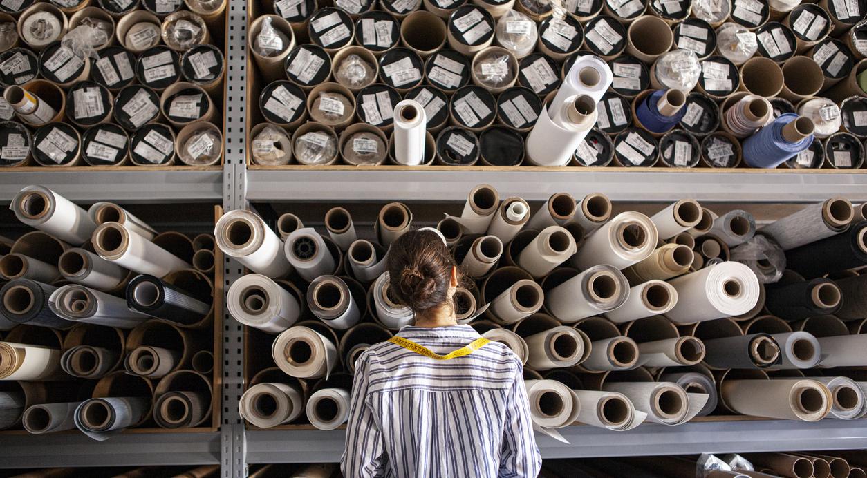 textile designer choosing fabric from stack of rolls inside sustainable workshop.