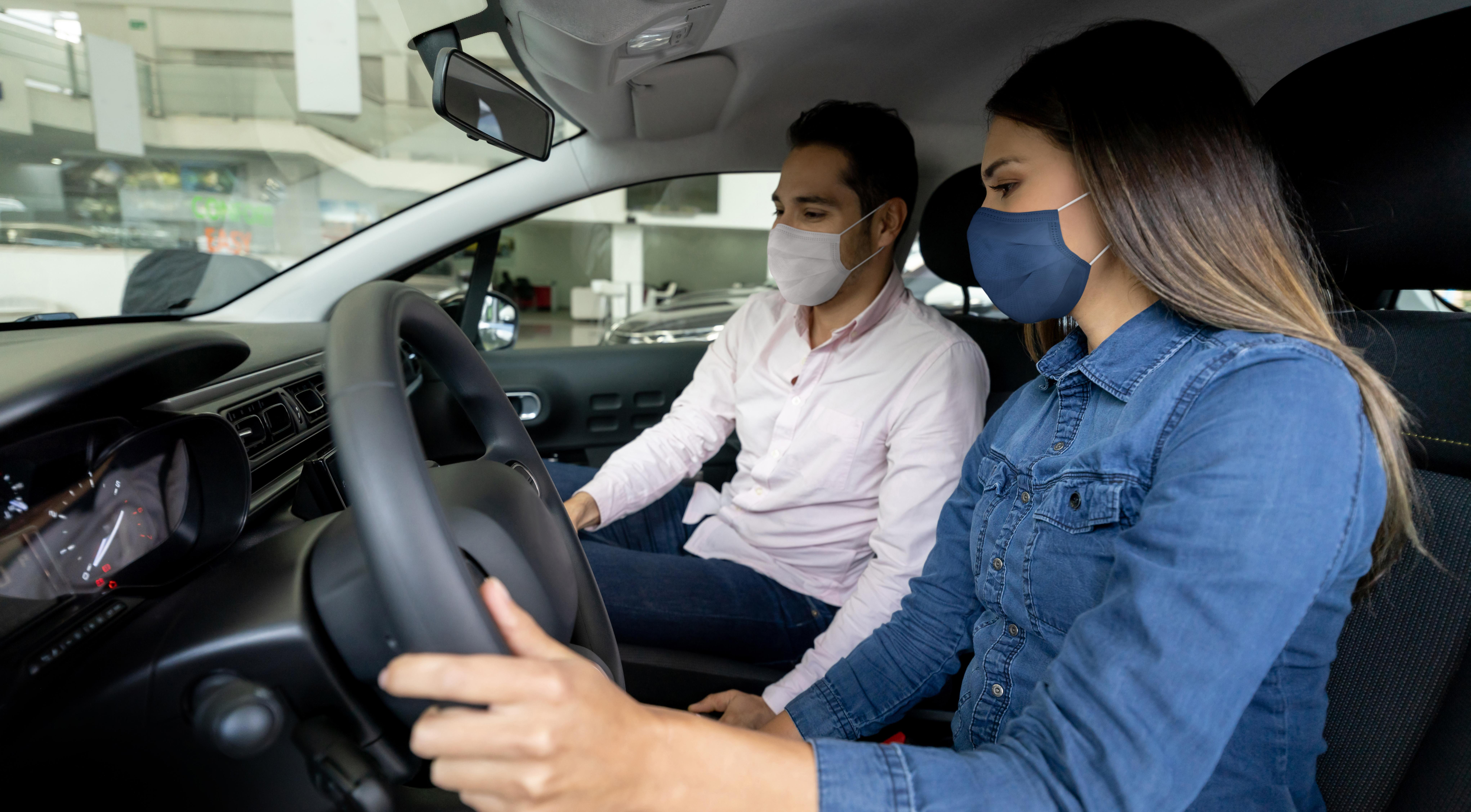 Woman talking to a salesman and wearing facemasks while buying a car at the dealership.