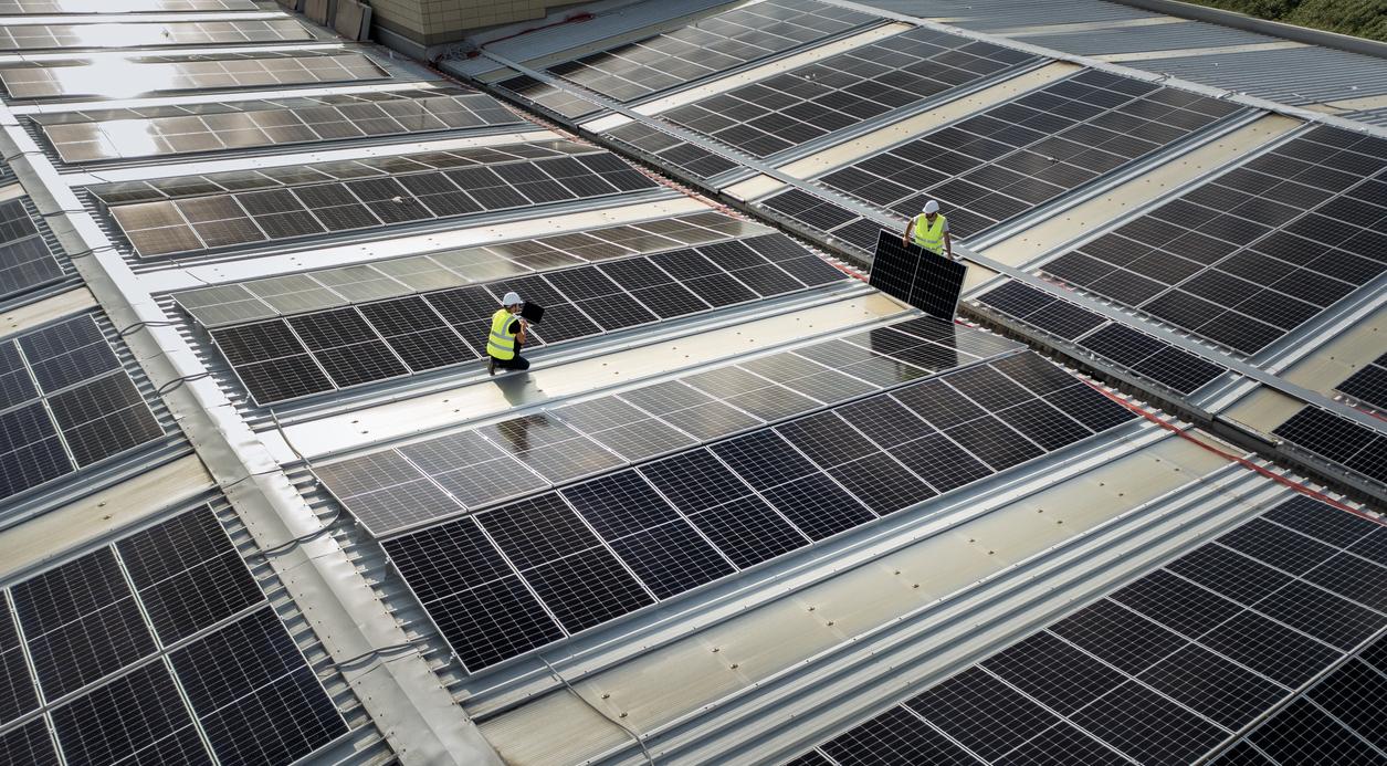 team of engineers using technology while installing solar panels on a roof of warehouse.